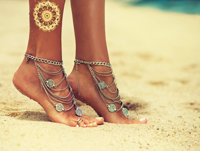Esta mujer lleva pulseras decorativas en su pies. Están abrochadas en el tobillo y también en uno de sus dedos del pie. Está en la playa y hace un día estupendo.