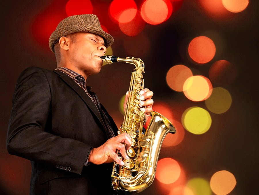 Este hombre está tocando su saxofon en un club de jazz. Lleva traje y sombrero elegante.
