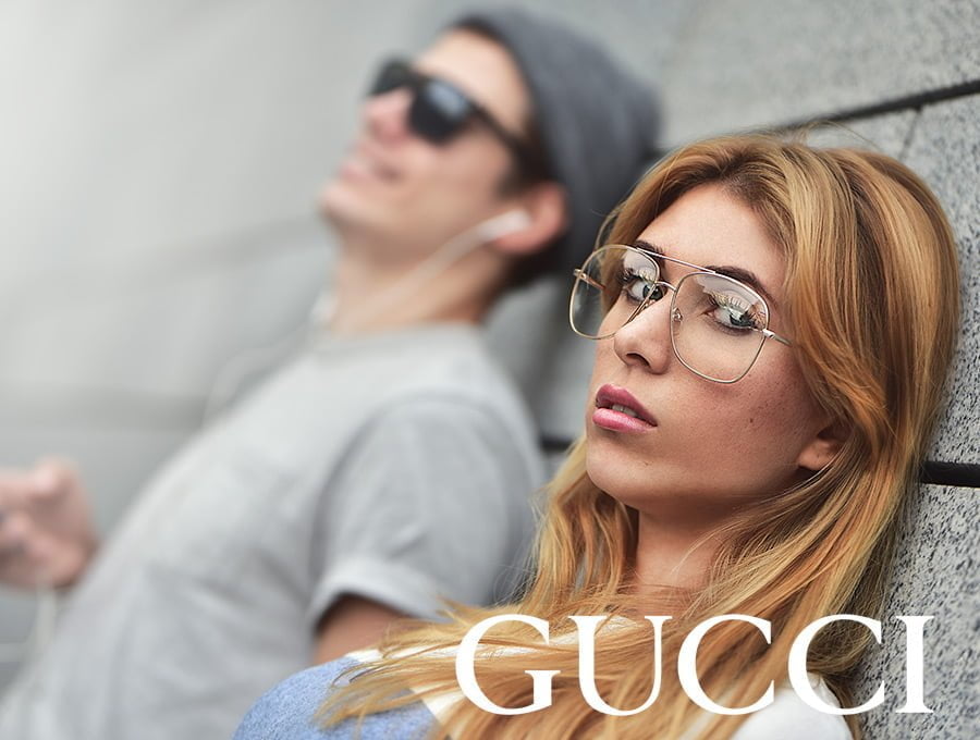 Esta pareja está apoyada en la pared de una calle. Ambos llevan fragancias de Gucci, además de algunas de sus prendas de vestir. El chico está escuchando música en su móvil, ella está mirando a la cámara.