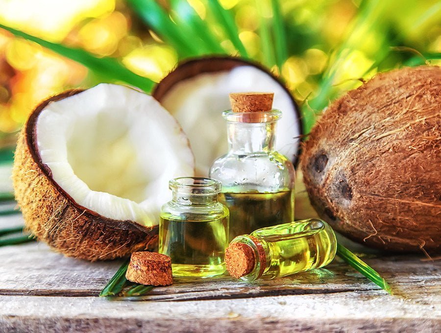 Tres frascos de cristal llenos de aceite esencial de coco. Se utilizará para elaborar perfumes de gran calidad con aroma a coco. También hay varios cocos a los lados.