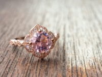 Anillo de oro rosa con diamantes ensartados de pequeño tamaño y una morganita en el centro. Es una pieza de joyería muy lujosa y cara. El anillo de compromiso está sobre la mesa.