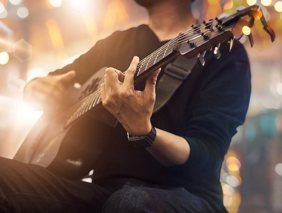 Este artista está tocando la guitarra delante del público en un festival de música. Hay muchas luces y la guitarra es de color negro.