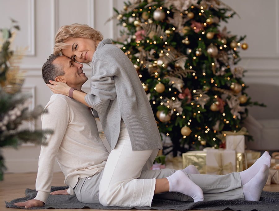 Un matrimonio sentados en una manta delante del arbol de navidad. Parece que están en modo romántico.