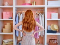 Esta mujer joven está mirando el armario de la ropa y los complementos. Quiere ordenarlo con un estilo minimalista para encontrar mejor la forma de vestirse. Tiene el color de pelo pelirrojo.