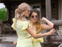 Dosc chicas con su bonito vestido amarillo de tono claro, se sacan un selfie. Llevan joyas plateadas para combinar con el amarillo claro del vestido.