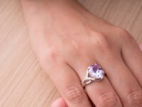 Mano de una mujer llevando un anillo chapado en plata de bisutería con una gema en uno de sus dedos.