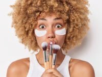 Esta mujer de piel morena tiene varias brochas de maquillaje en sus manos. No sabe cuál utilizar para maquillar su piel afroamericana.