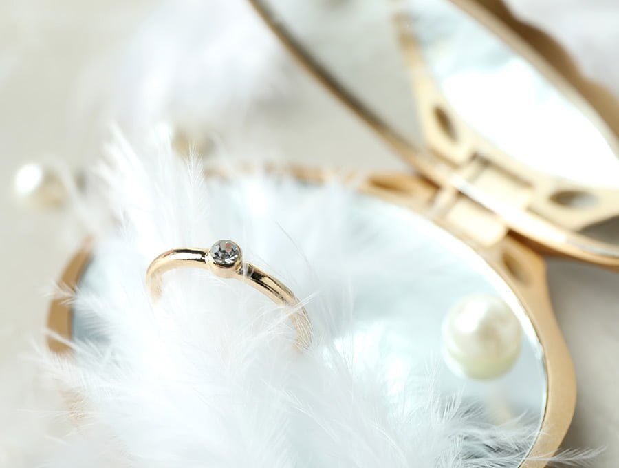Un anillo de oro amarillo con un diamante en bruto engastado. Hay algunas plumas de ave blancas decorativas.