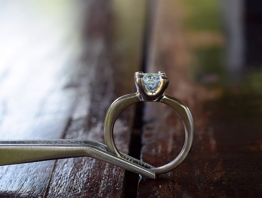 Este joyero nos muestra un anillo cogido con pinzas. El anillo es de oro blanco y tiene un diamante en bruto.