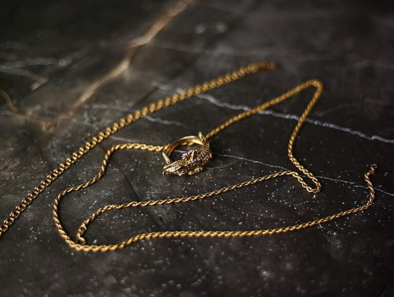 Una cadena de oro fino junto a un anillo encima de una mesa de mármol.