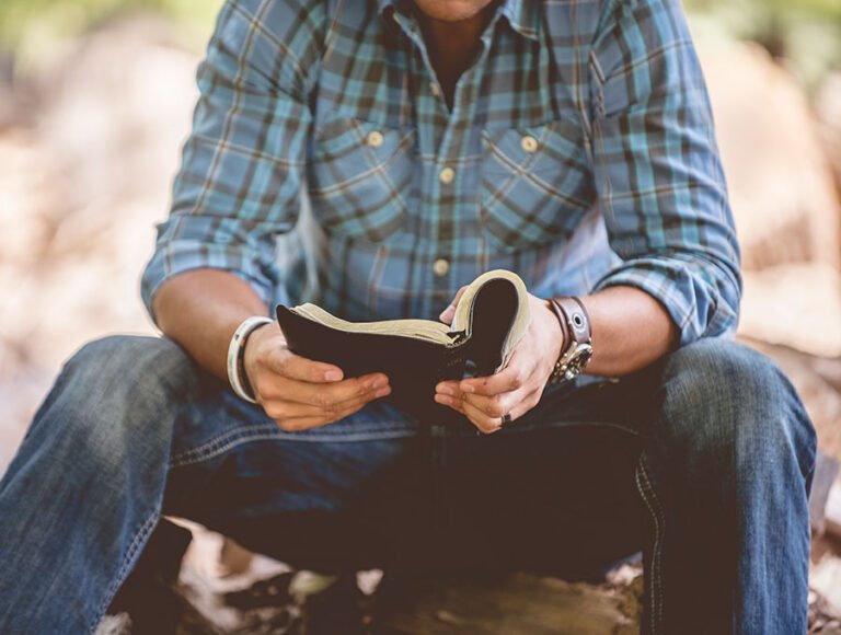 Hombre con vaqueros leyendo la biblia con detenimiento.