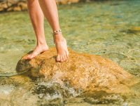 Mujer sobre una roca en la playa. Lleva dos pulseras tobilleras.