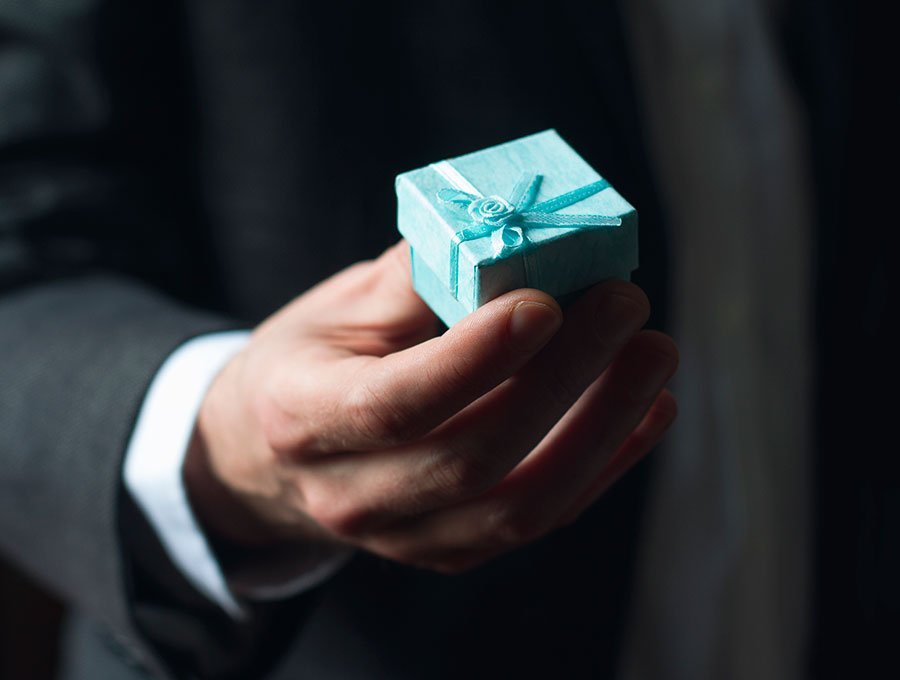 Hombre sostiene una cajita de regalo con anillo de compromiso en su interior.