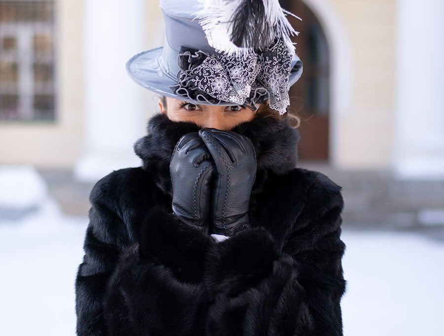 Mujer con ropa de abrigo y sombrero de época. Está en la ciudad nevada.