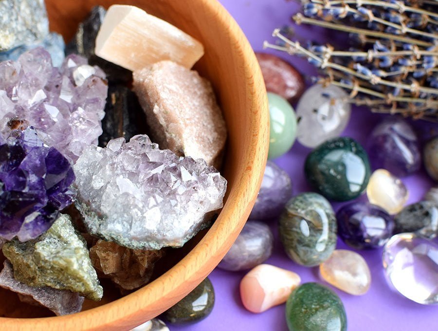 Piedras y cristales naturales de distintos colores dentro de un cuenco de madera y sobre la mesa.