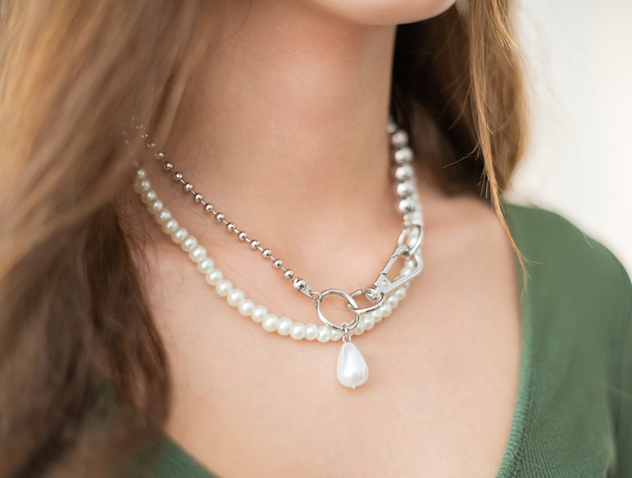 Mujer lleva un collar de perlas y otro de plata.