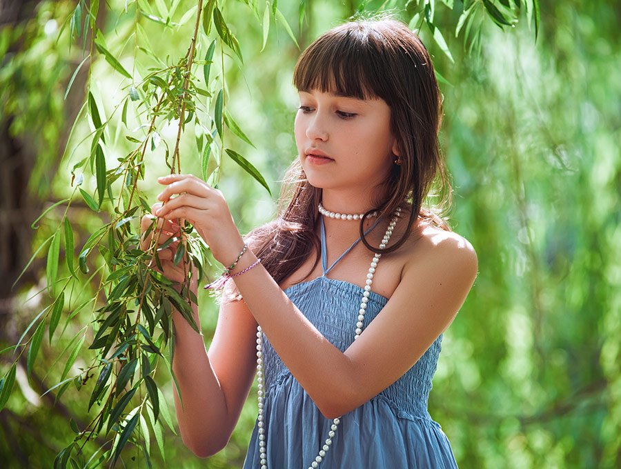 Niña juega con las hojas del árbol del jardín, mientras lleva puesto el collar de perlas de su madre.